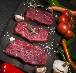 Raw beef steak on a cutting board with rosemary and spices.