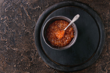 Bowl of red caviar with spoon served on black wooden chopping board over brown texture background. Top view with space