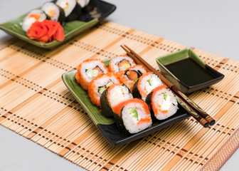 Japanese sushi and rolls with ginger in colored tableware with chopsticks on the Mat