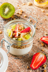 Healthy breakfast. Diet. Overnight oatmeal in a can, muesli. Yogurt with homemade granola and organic fruits - kiwi, banana, strawberry. On the stone table. With ingredients and spoons. 