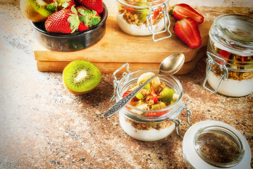 Healthy breakfast. Diet. Overnight oatmeal in a can, muesli. Yogurt with homemade granola and organic fruits - kiwi, banana, strawberry. On the stone table. With ingredients and spoons. 