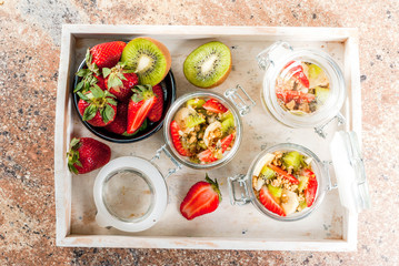 Healthy breakfast. Diet. Overnight oatmeal in a can, muesli. Yogurt with homemade granola and organic fruits - kiwi, banana, strawberry. On the stone table. With ingredients and spoons. 