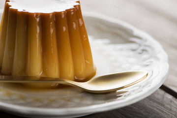 Close-up of plate with flan and spoon on the wooden background. Horizontal shoot.