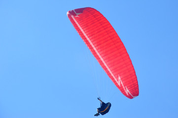 The pilot controls the red paraglider in the sky
