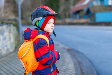 Cute little preschool kid boy riding on scooter riding to school.