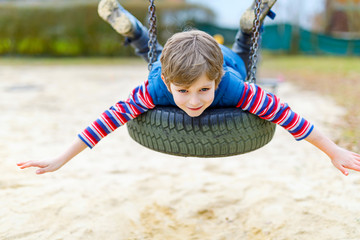 Funny kid boy having fun with chain swing on outdoor playground