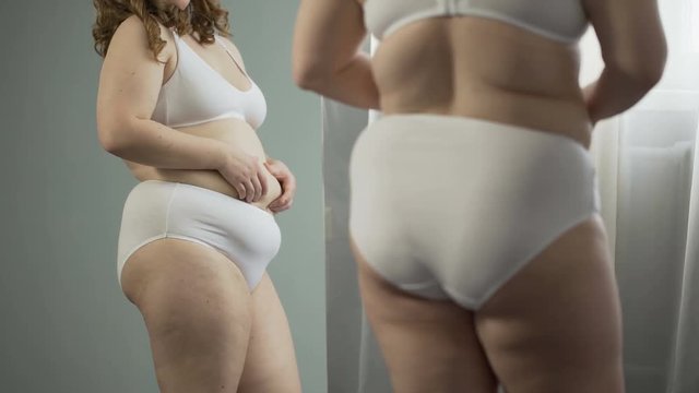 Young woman looking at fat belly, wants to lose excess weight, risk of diseases