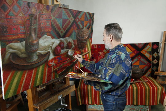 Adult painter draws the ethnical still life picture by oil paint in art workshop