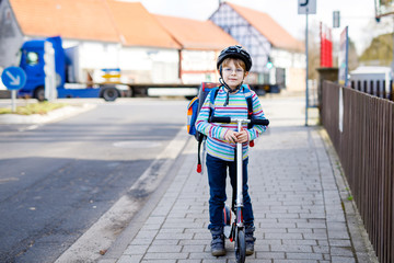 Fototapeta premium Little kid boy in helmet riding with his scooter in the city