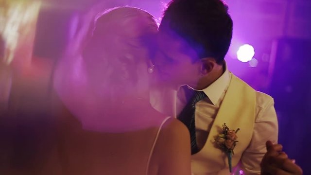 Violet lights illuminate gorgeous wedding couple dancing in the restaurant