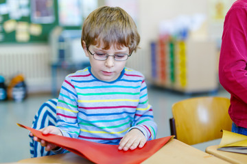 school kid boy with glasses playing with colorful paper and making geometric figures