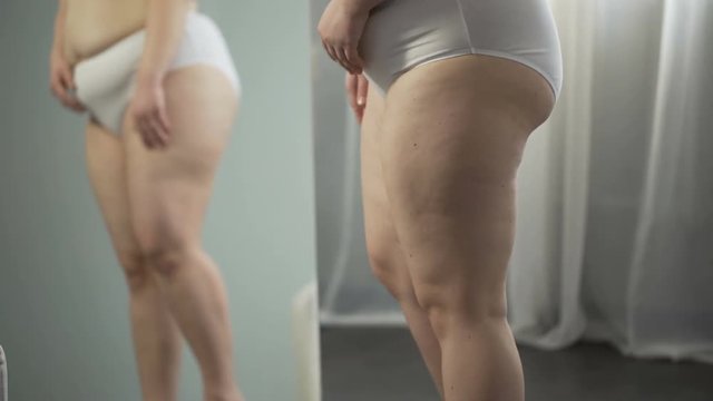 Woman looking in mirror, cellulite and stretch marks on hips, touching big belly
