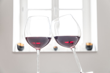 Zwei Gläser mit Rotwein auf einem weißen Tisch vor weißem Hintergrund und Fenster