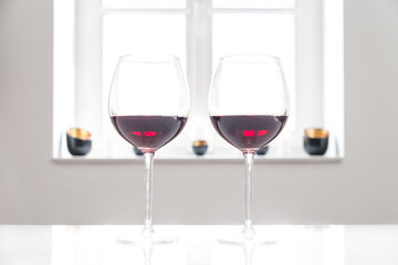 Zwei Gläser mit Rotwein auf einem weißen Tisch vor weißem Hintergrund und Fenster