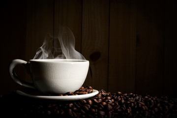 Steaming coffee cup put on coffee beans on wood background.