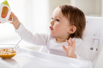 baby drinking from spout cup in highchair at home