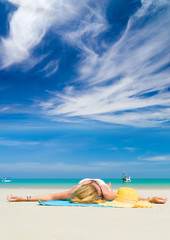 Fototapeta na wymiar Woman lies on the beach with yellow hat and towel
