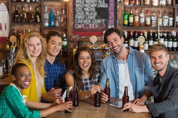 Portrait of cheerful young friends with beer bottles in pub