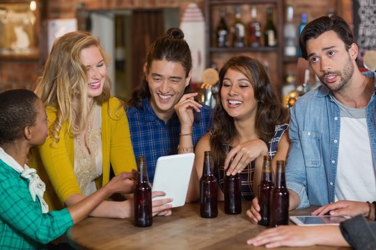 Happy friends with beer bottles using digital tablet