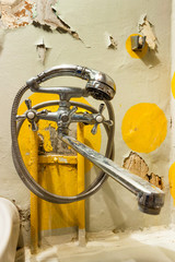 Old rusty shower tap on the background of a painted concrete wall with cracked paint. Poverty