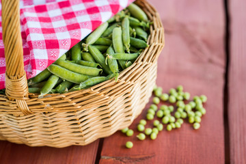 Unopened pea pods in a basket on wooden background.