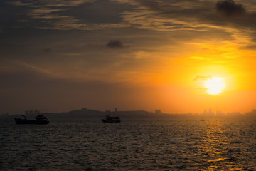 Naklejka na ściany i meble Sunset on the sea. Silhouette of city and fishing boat