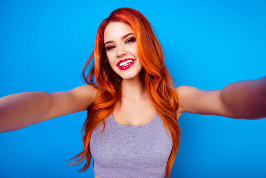 Portrait of stylish funny happy carefree girl with ginger hair,cute face and big breast make selfie photo and laugh while standing on blue background
