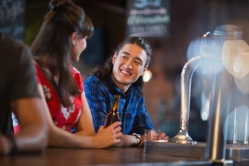 Happy friends looking at each other while leaning on bar counter