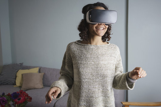 Happy woman using virtual reality headset while standing in living room