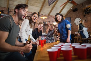 Young friends enjoying beer pong game in restaurant - obrazy, fototapety, plakaty