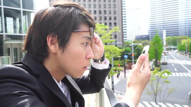 ビジネスマン　スマホを見て驚く　眼鏡を上げる