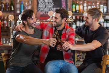 Happy young male friends toasting beer bottles in bar