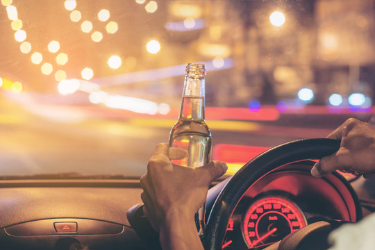 Drunk young man driving a car with a bottle of beer. Don't drink and drive concept. Driving under the influence. DUI, Driving while intoxicated.