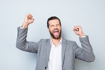 Yes! Young excited screaming man in suit with raised hands depicted on gray background