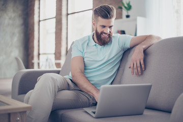 Young bearded man is making shopping online sitting at home on the cozy sofa