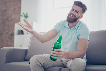 Upset young man is frustrated about the loss of the team in game he is watching. Guy is having beer and sitting on the sofa at livingroom