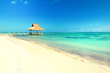 Tropical white sandy beach. Palm leaf roofed wooden pier with gazebo on the beach. Punta Cana, Dominican Republic