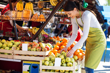 Young attractive fruit market saleswoman selecting fresh fruit and preparing for working day.