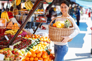 Young woman on street market holding basket  full of fruits and looking at camera. 