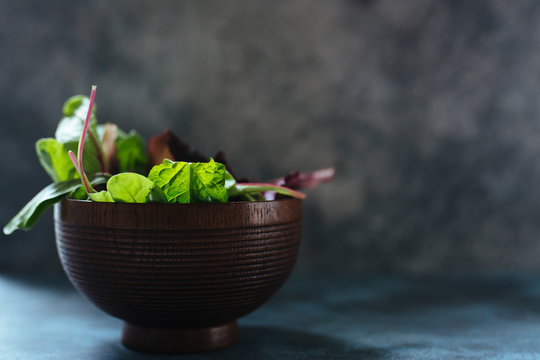 Varieties of lettuce, fresh holas in a wooden bowl over rustic texture