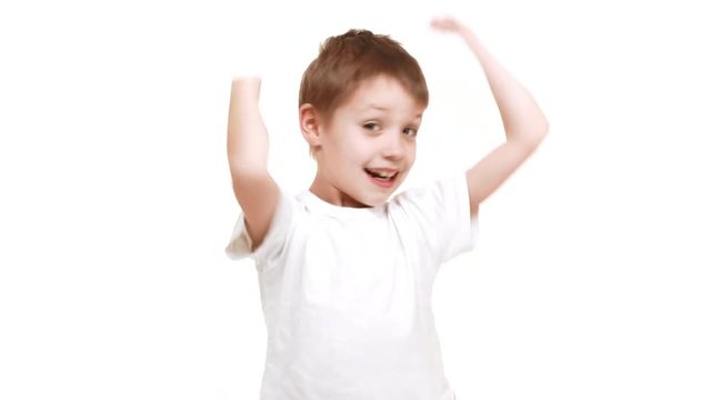 Very young cute Caucasian boy standing on white background and happily raising hands up in joy