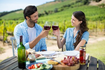 Smiling couple toasting red wine glasses while sitting at table
