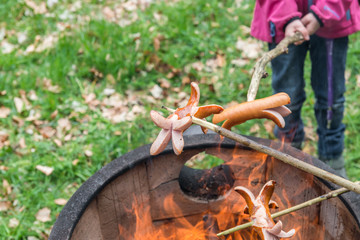 Ein Kind hält eine auf einen Stock aufgespießte Wurst in offenes Feuer eines Feuertopfs