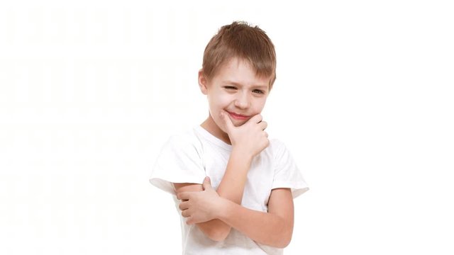 Thoughtful elementary-school aged Caucasian boy standing on white background slightly scratching chin