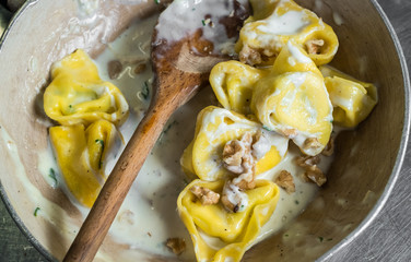 Tortelloni (typical Bologna homemade stuffed pasta) with nuts, cream and sage in their cooking pan 