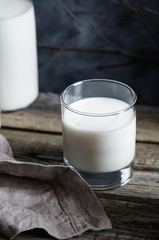 Close-up of a glass of milk on a rustic wooden table against the dark wall.