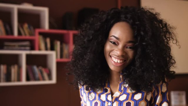 Portrait of a beautiful young afro american woman with curly hair turns her head looking into the camera and smiling in a cafe