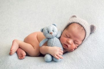 Newborn boy in a naked hat lies on a light blanket with a blue knitted bear