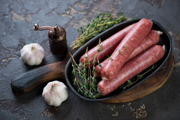 Wooden serving board with raw marbled beef sausages in a frying pan and seasonings, studio shot