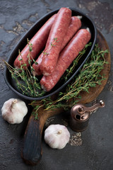 Frying pan with uncooked marbled beef sausages, fresh thyme and garlic over dark brown stone background, vertical shot